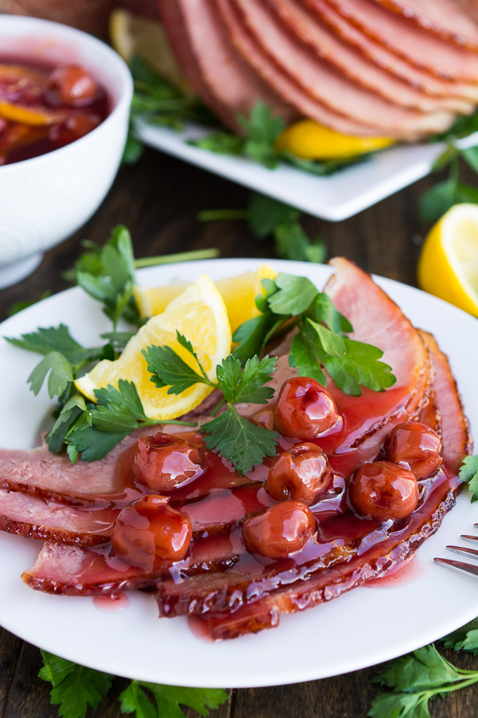 a plate with sliced ham, topped with cherries, a lemon wedge and parsley