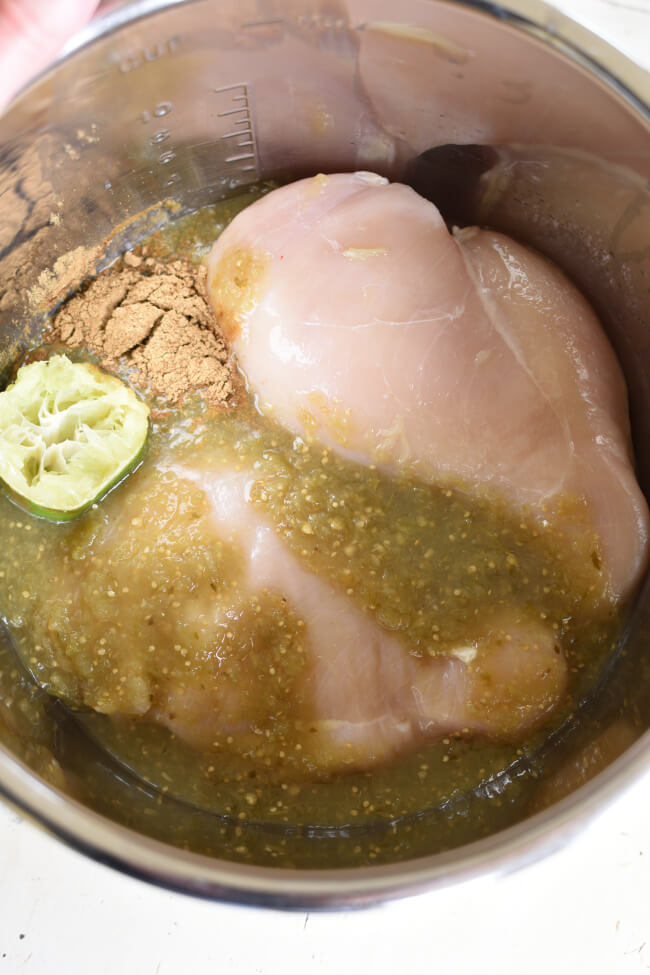 two raw chicken breasts smothered in verde, cumin, and a lime wedge