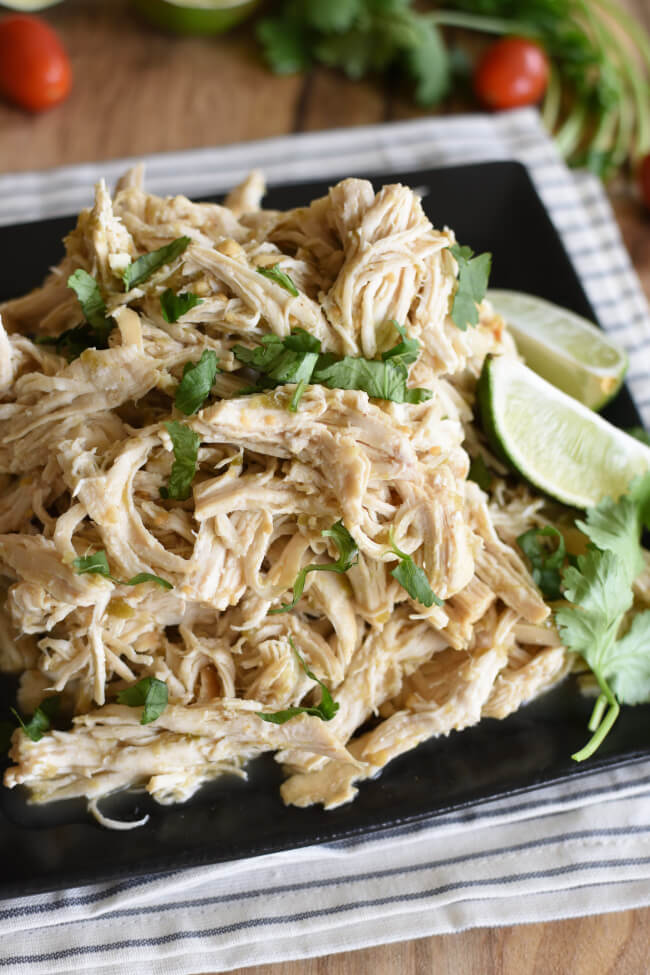 a black plate with shredded chicken breasts sprinkled with chopped cilantro