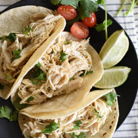 birds eye view of three shredded chicken tacos with lime wedges and cilantro