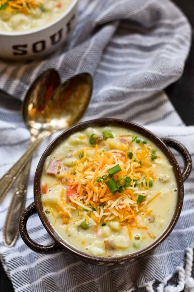 a black bowl with potato soup topped with chives and cheese