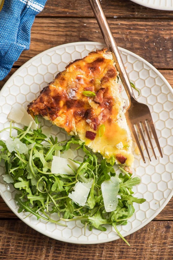 a wedge of baked quiche and a green salad on a plate with a fork