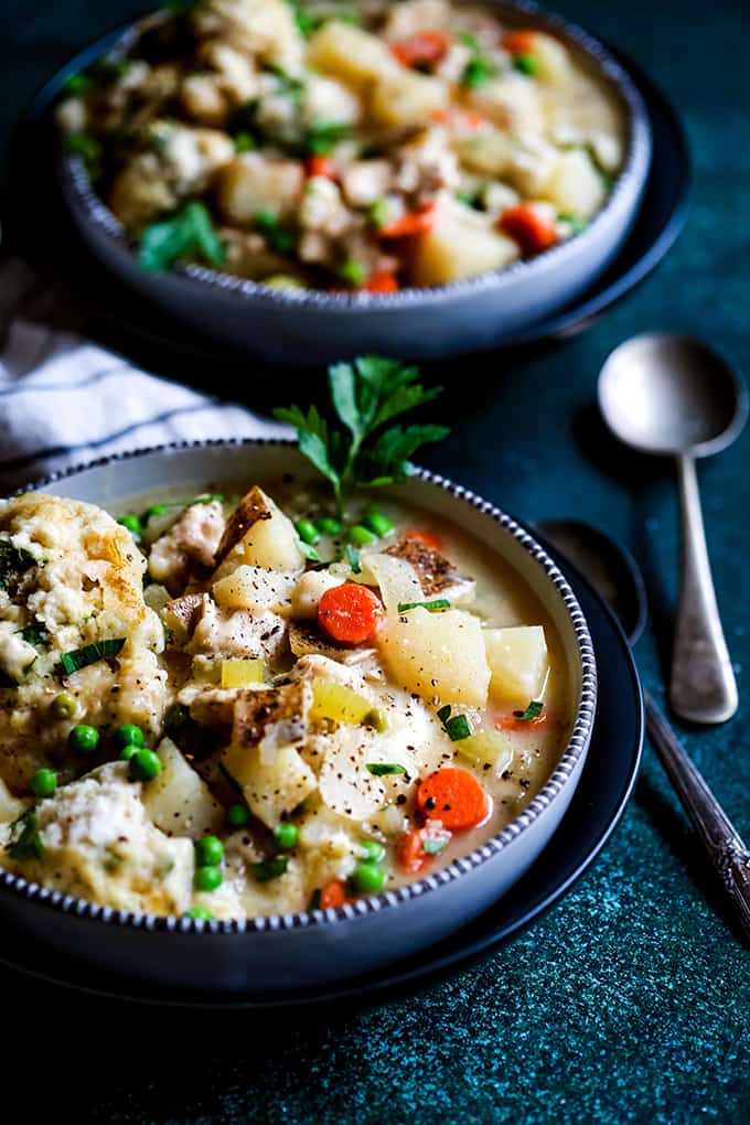 two bowls of chicken and dumplings soup with peas, carrots, and parsley