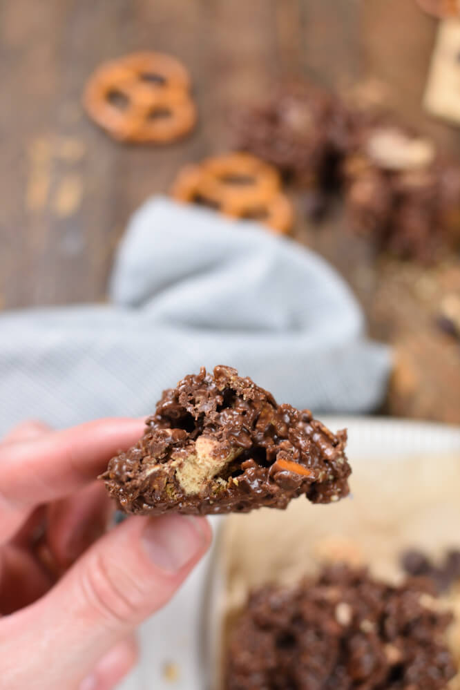 a hand holding a no bake cookie with a bite taken out of it. Pretzels in the background