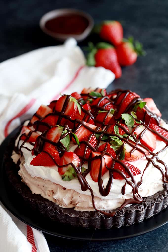a chocolate tart topped with whipped cream, fresh strawberries, and drizzle of chocolate sauce