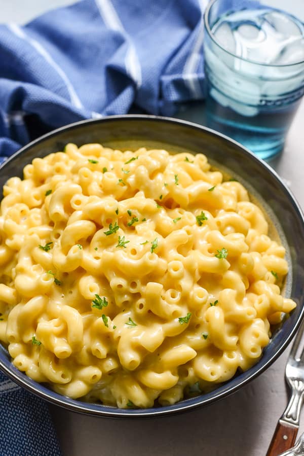 a black bowl with mac and cheese topped with chopped parsley