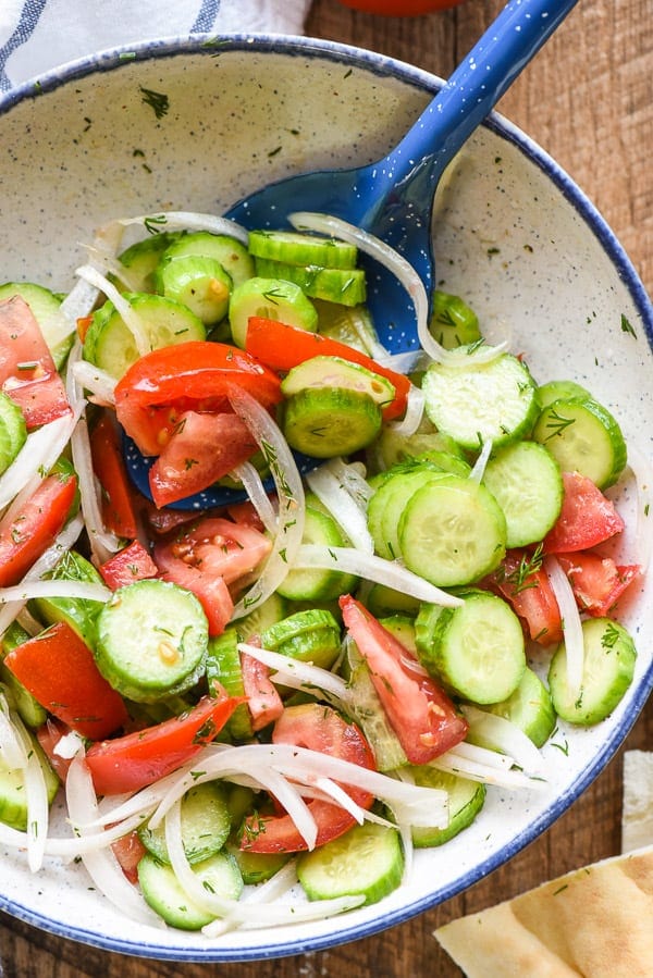 a white bowl with sliced cucumbers, tomatoes, and sliced onions