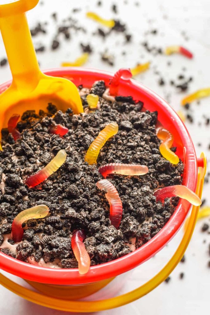 a red plastic bucket filled with chocolate pudding and covered with Oreo cookie crumbs and gummy worms.