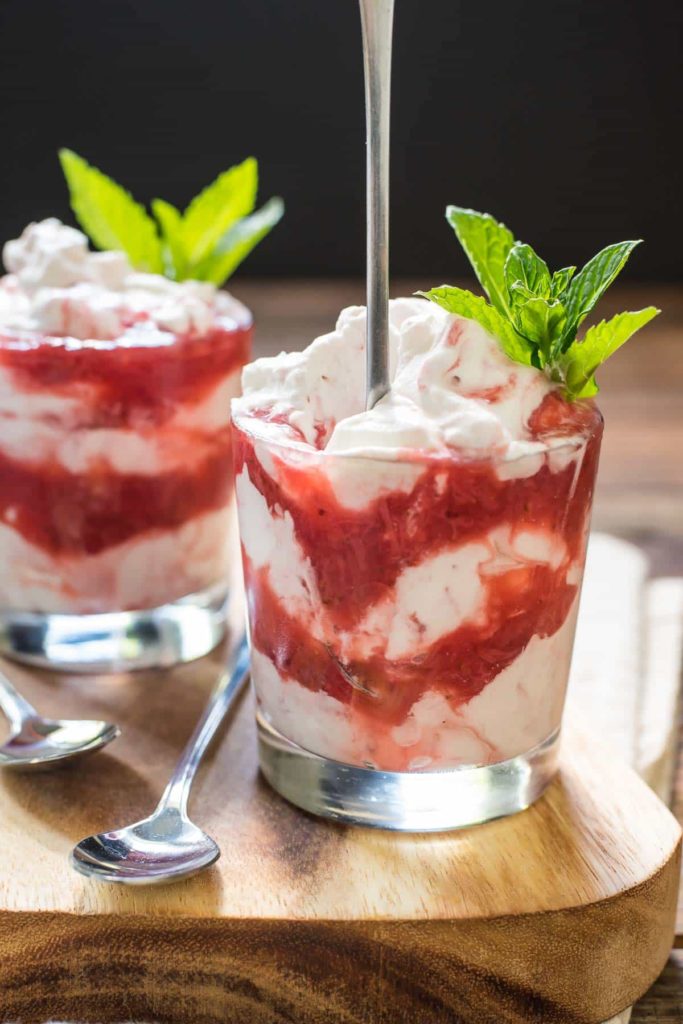 a glass cup with layers of red strawberry sauce and white cream topped with mint