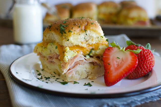 a white plate with a baked ham egg and cheese breakfast slider and a sliced strawberry