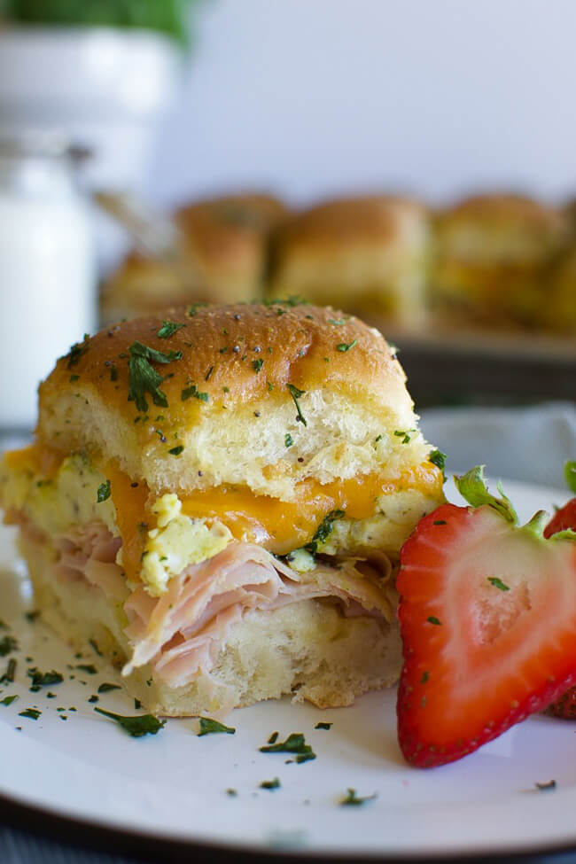 a white plate with a baked ham egg and cheese breakfast slider and a sliced strawberry