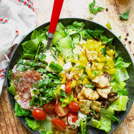 a black bowl with lettuce, olives, tomatoes, and salami