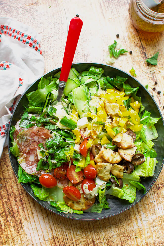 a black bowl with lettuce, olives, tomatoes, and salami