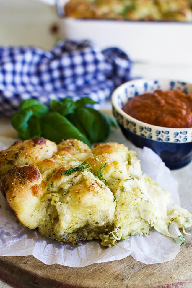 pieces of monkey bread on a white napkin with a dish of marinara sauce and basil