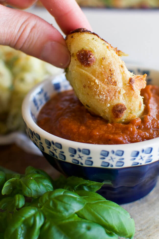 a piece of pull apart bread being dipped in marinara