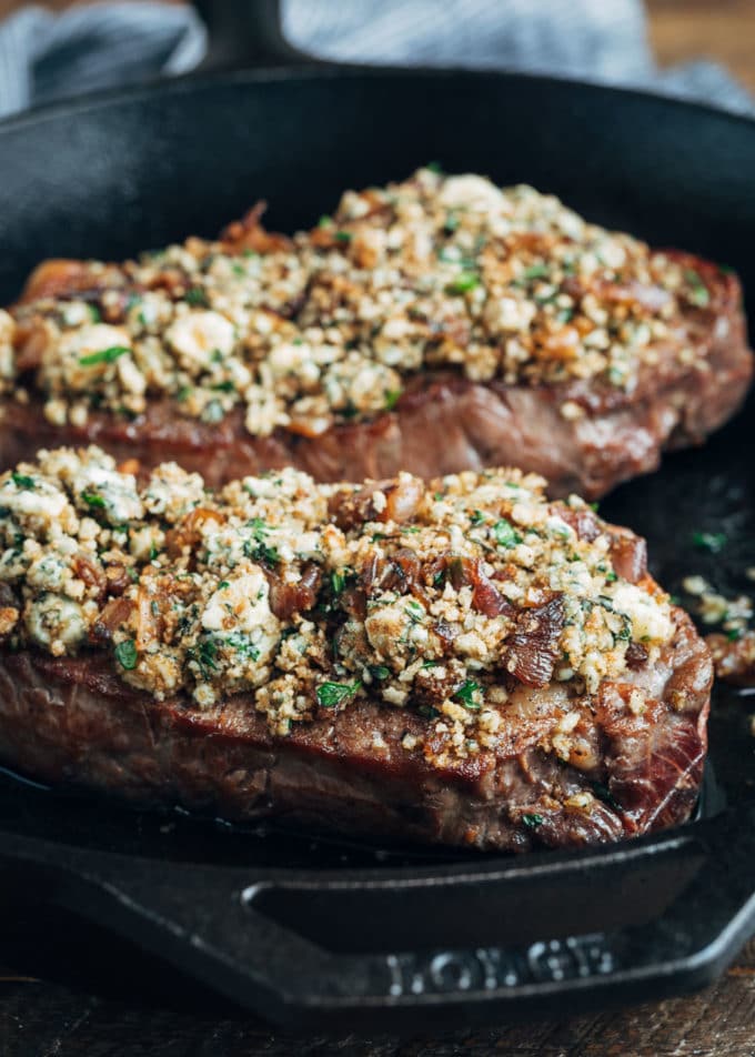 a black plate with two seared steaks crusted with cheese