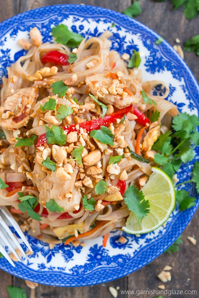 a plate with thai chicken, lime slices, and noodles