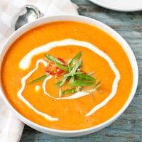 a bowl of orange tomato soup fresh basil and cream