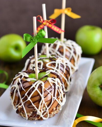 three caramel coated apples drizzled with white and semi sweet chocolate. Apples are on a stick with ribbons tied on top