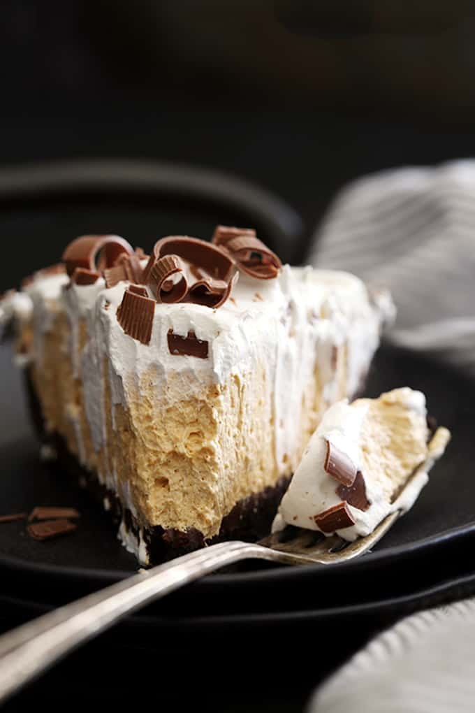 a wedge of pumpkin cheesecake in a chocolate crumb crust, topped with whipped cream and chocolate curls with a fork and a bite