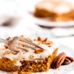 a square of pumpkin cake topped with chopped walnuts and white frosting, and a fork taking a bite