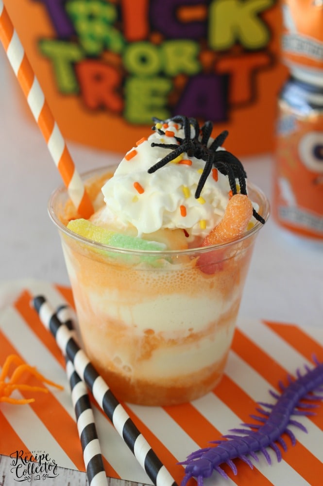 orange soda and vanilla ice cream float topped with gummy worms, whipped cream, a plastic spider, and an orange and white paper straw