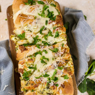 an flat lay image of pull apart spinach and artichoke bread on a wooden cutting board with parsley and grated cheese