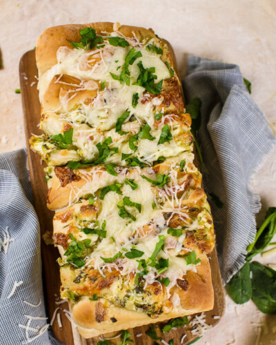 an flat lay image of pull apart spinach and artichoke bread on a wooden cutting board with parsley and grated cheese