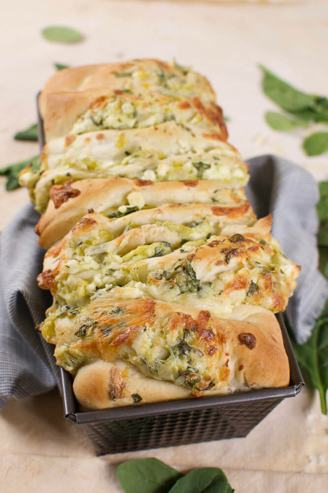 a black bread pan with baked monkey bread stuffed with spinach and artichoke dip