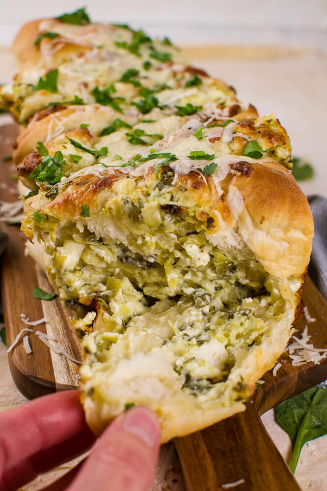 a loaf of pull apart bread with baked spinach artichoke dip stuffed inside