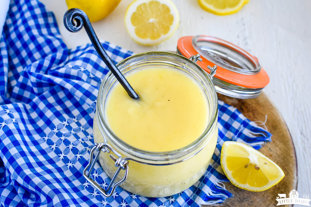 homemade lemon sauce in a mason jar with a black spoon and lemons in the background.  Little Dairy on the Prairie