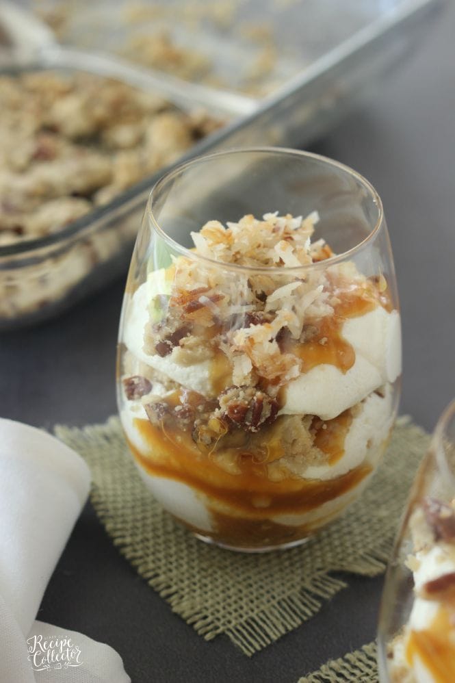 a glass with layers of cream, coconut, nuts, and caramel drizzled over the top