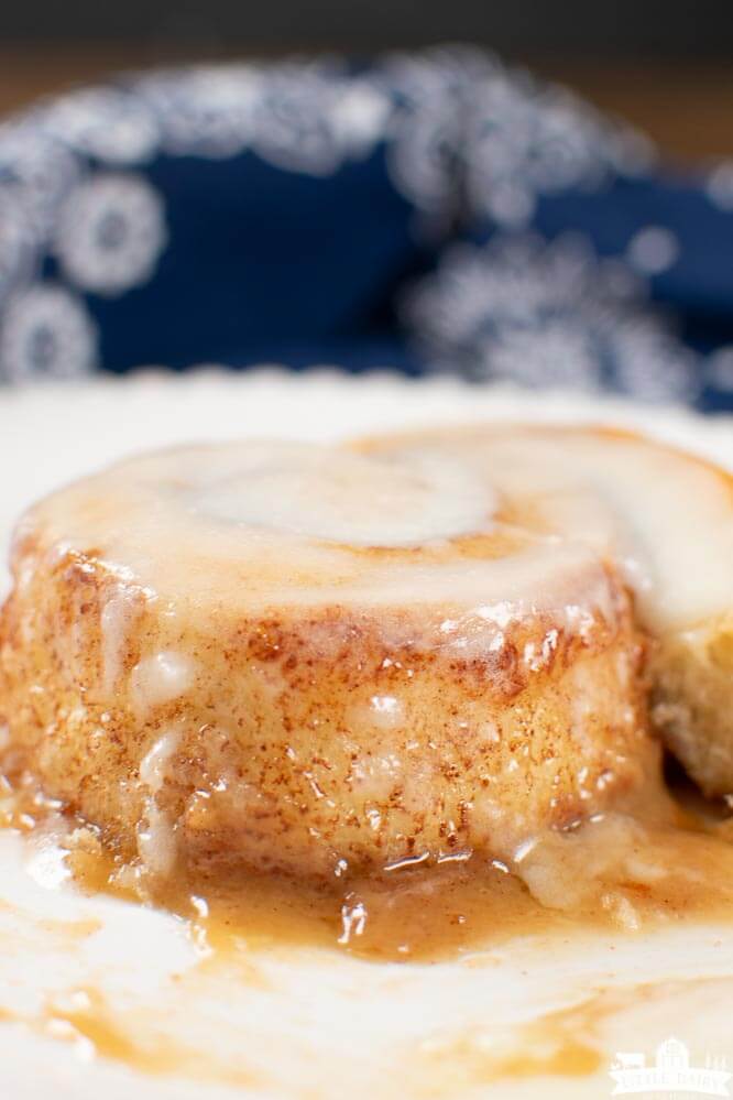 an unrolled cinnamon roll nestled in golden brown caramel sauce and frosted with cream cheese icing.