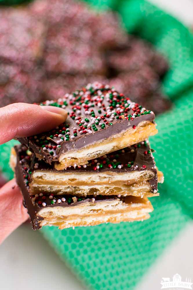 fingers holding three pieces of candy made with saltine crackers and topped with chocolate and sprinkles