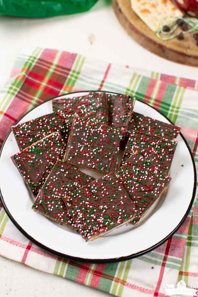 a black rimmed, white plate with squares of saltine cracker toffee stacked on it.