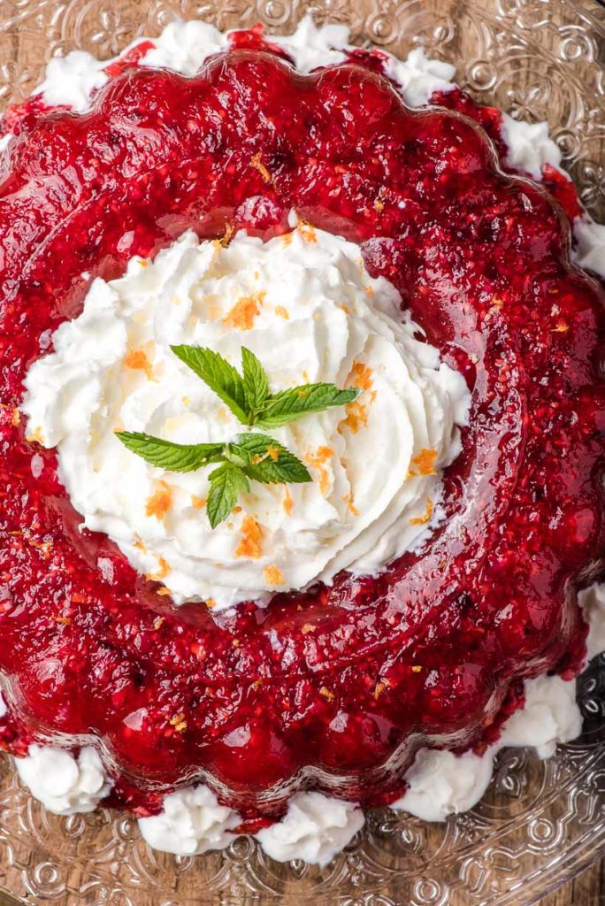 red jello with fruit shaped in a ring, filled with whipped cream and topped with mint leaves