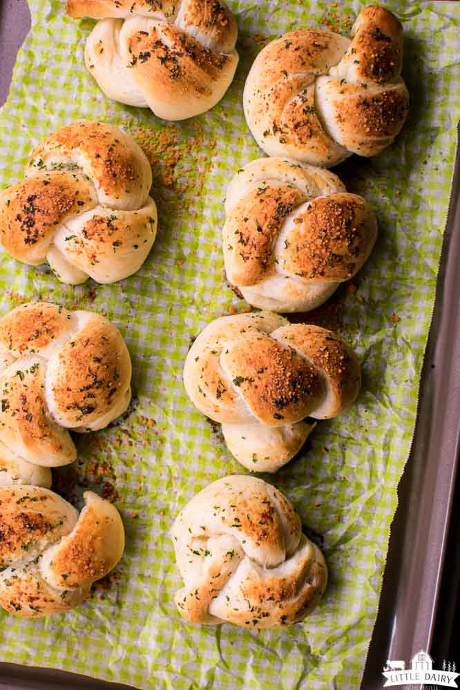 a sheet pan of homemade baked bread knots sprinkled with parmesan cheese