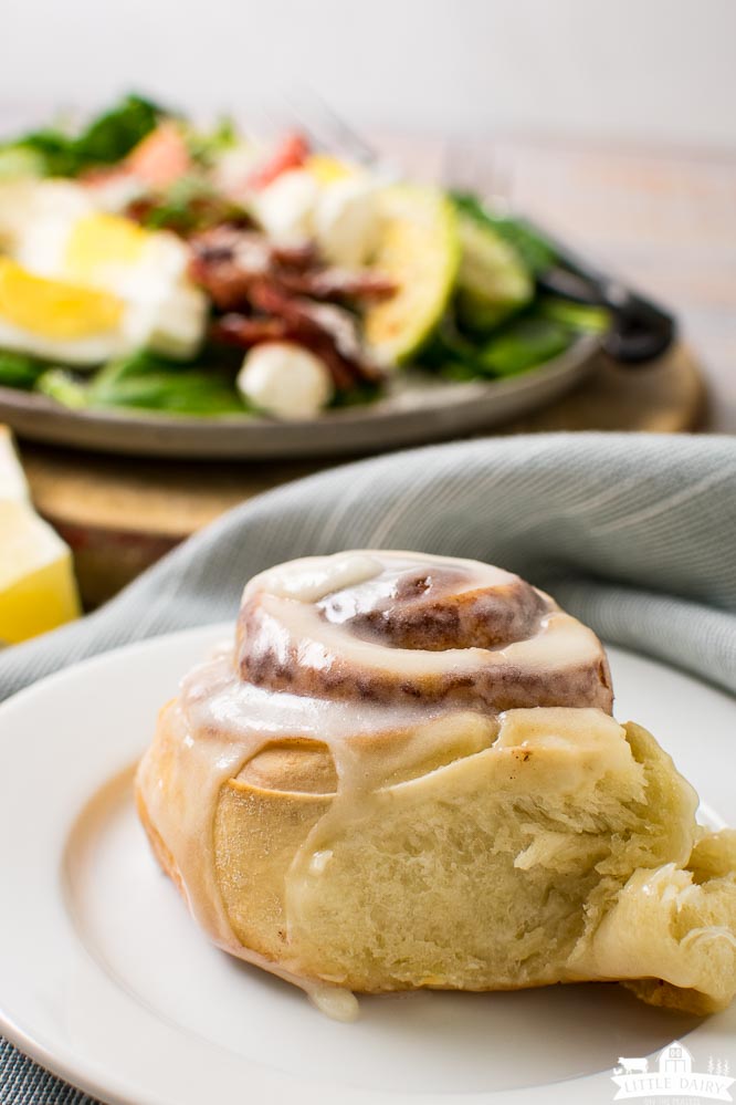 a cinnamon roll with icing and a breakfast salad in the background