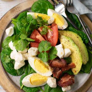 A healthy, savory breakfast salad with layers of spinach, eggs, tomatoes, cheese, avocado, and bacon.