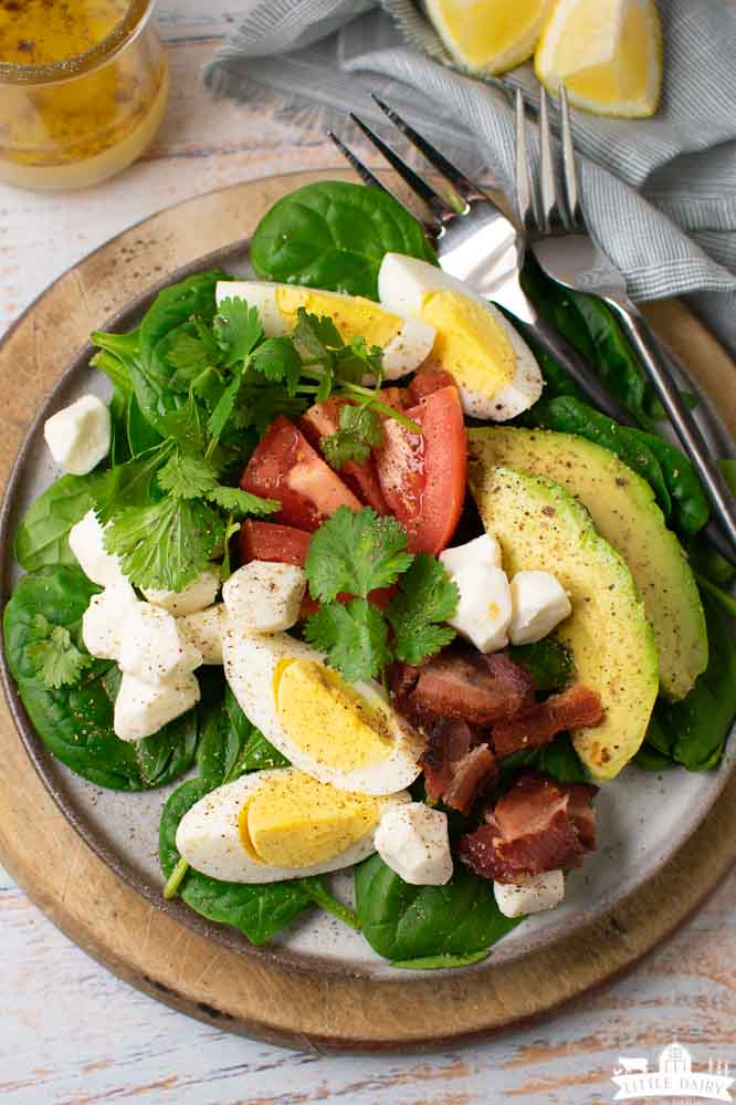 A healthy, savory breakfast salad with layers of spinach, eggs, tomatoes, cheese, avocado, and bacon.