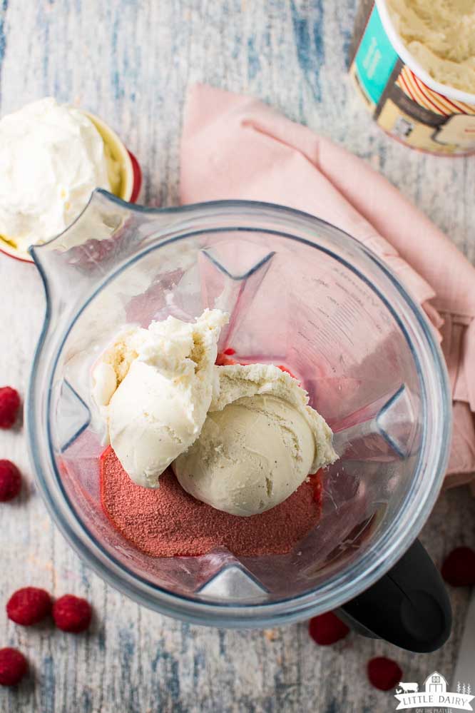 a blender with scoops of vanilla ice cream and dry jello mix, raspberries scattered around