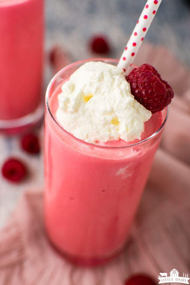 raspberry milkshake topped with whipped cream and a fresh raspberry with a red and white straw
