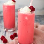 two glasses filled with fruity milkshakes, topped with whipped cream and a fresh raspberry