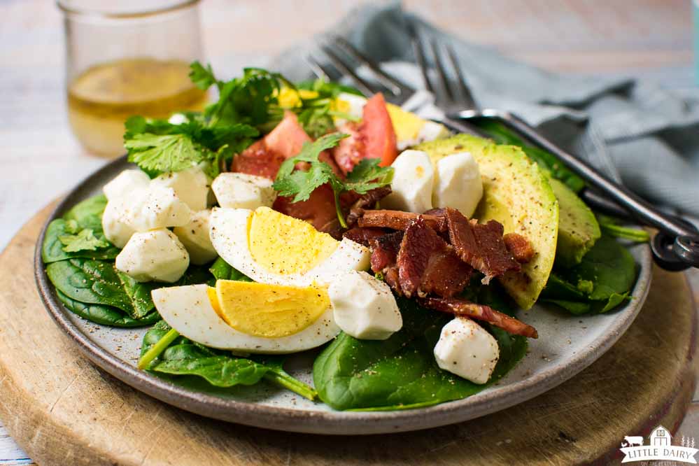 a plate with a savory breakfast salad loaded with eggs, bacon, and other breakfast vegetables