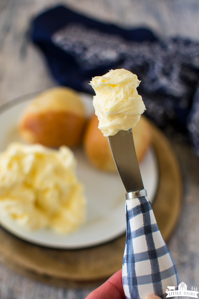 a blue and white checkered knife with soft and cream butter on it. Rolls are in the background