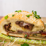 a slice of cheesesteak stromboli rolled up with layers of cheese, steak, and peppers and onions