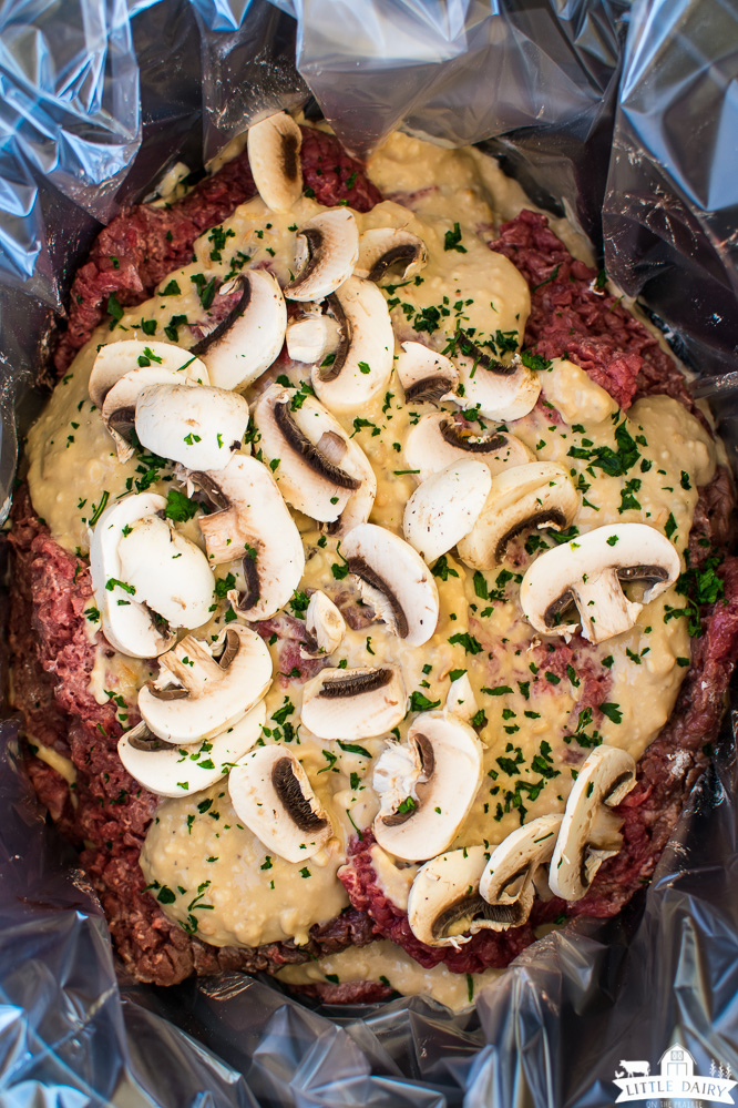 a crock pot with raw cubed steaks, mushroom gravy, and sliced mushrooms