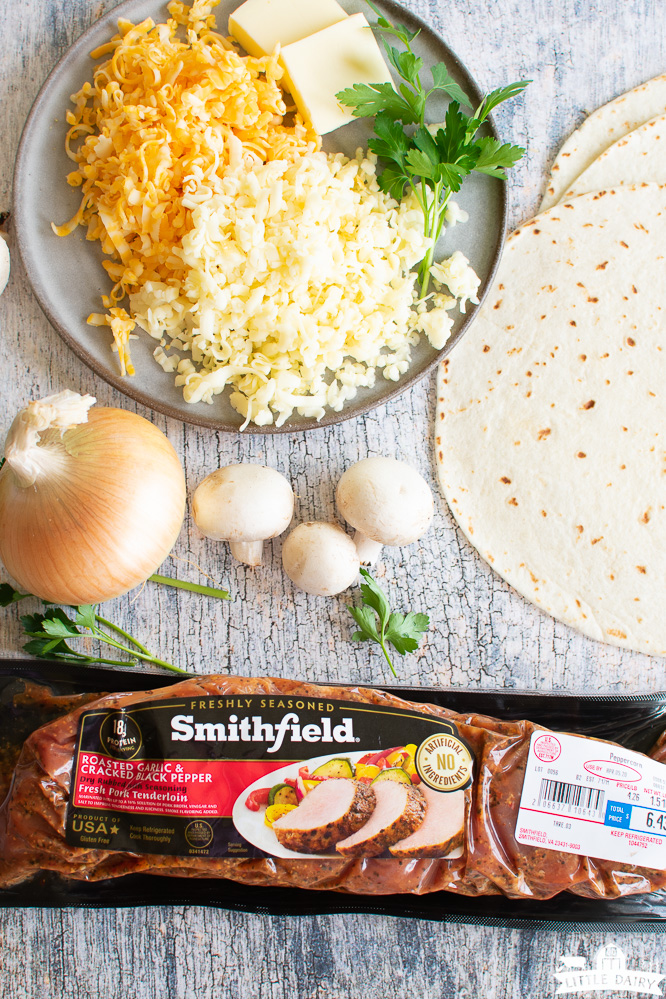 piles of cheese, flour tortillas, mushrooms, an onion, and a pork tenderloin