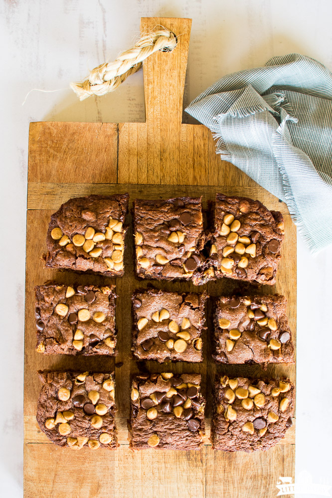 a wooden cutting board with nine squares of chocolate brownies with peanut butter chips and chocolate chips on top
