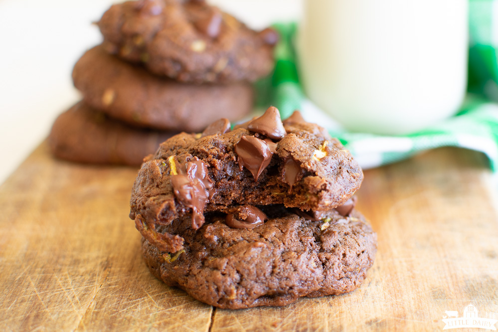a stack of two chocolate zucchini cookies with chocolate chips on a wooden board with a glass of milk in the background